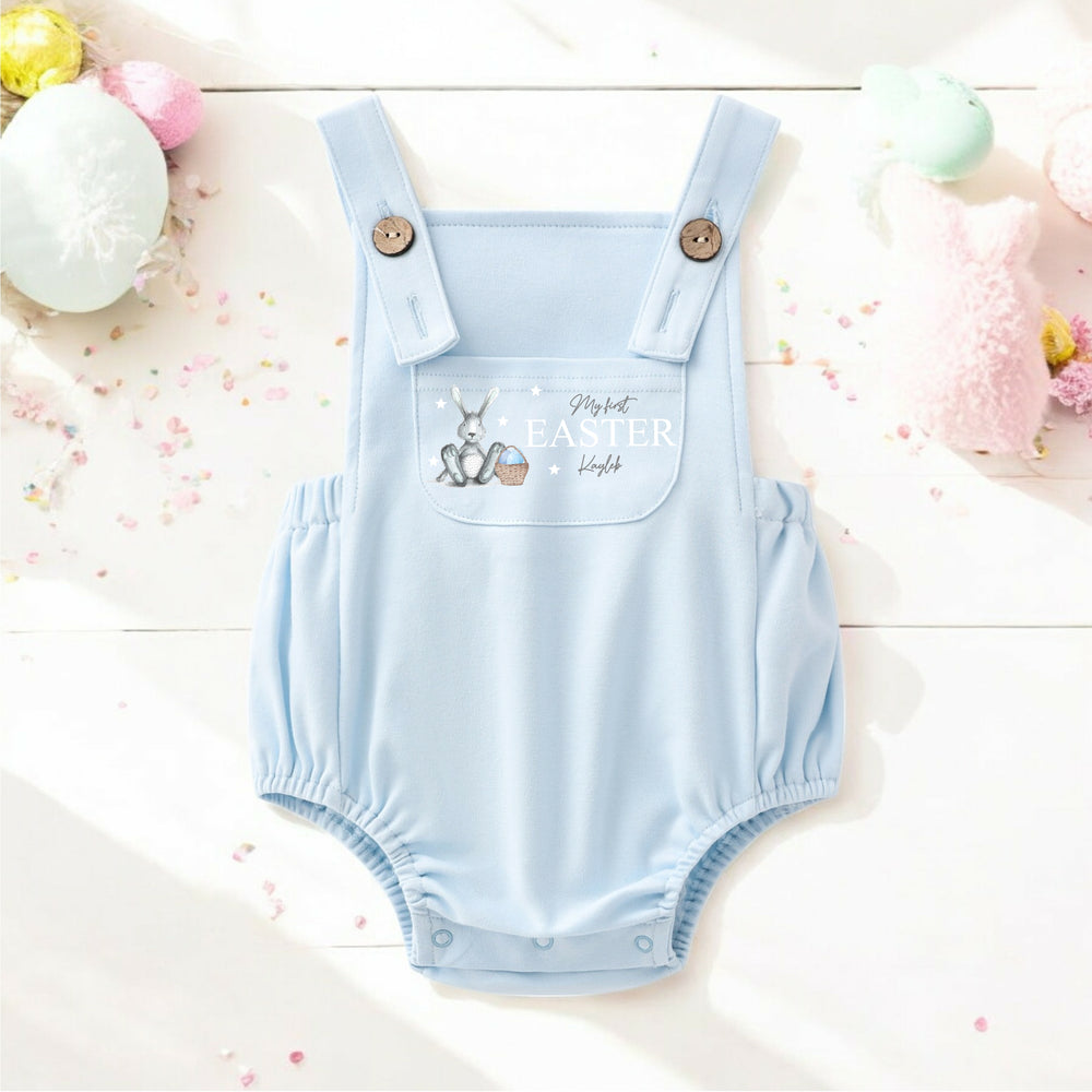 Persoanlised blue Easter dungarees that say 'My First Easter Kayleb'. This design features a grey bunny with blue details sitting next to an Easter basket full of eggs