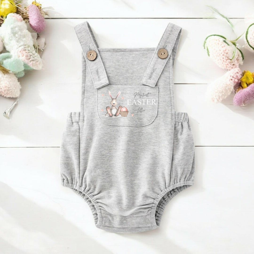 Persoanlised grey Easter dungarees that say 'My First Easter Lillie'. This design features a grey bunny with pink details sitting next to an Easter basket full of eggs