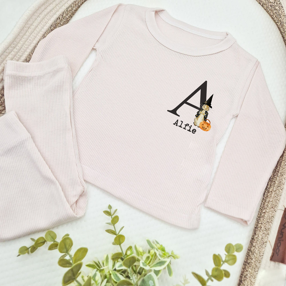 Pink baby outfit with 'Alfie' and a pumpkin design on a white surface with green leaves.
