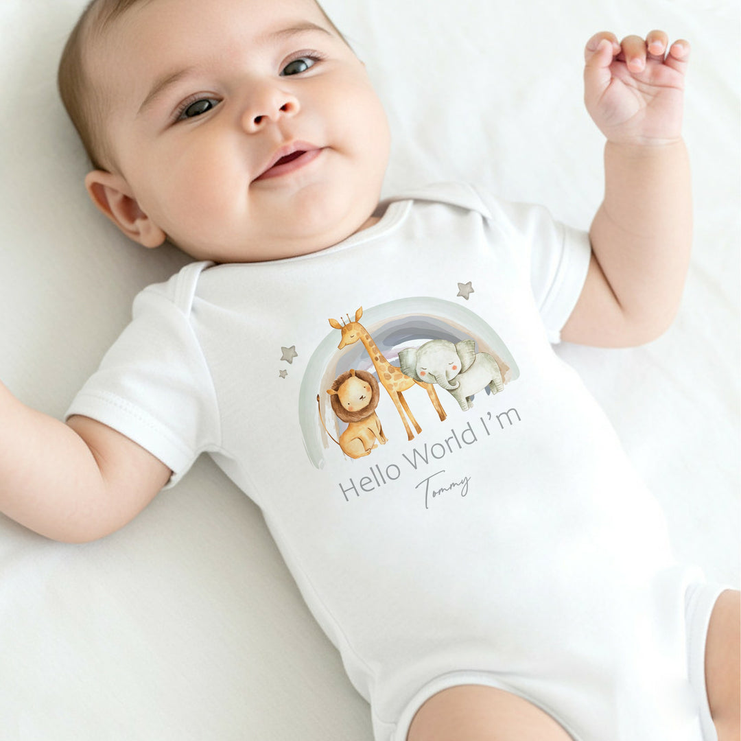 A personalised white baby vest that says 'Hello World I'm Tommy'. This design features a water colour rainbow with a lion, giraffe and a lion standing in front of it 