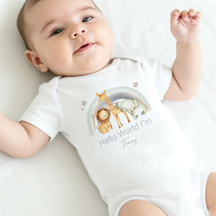 A personalised white baby vest that says 'Hello World I'm Tommy'. This design features a water colour rainbow with a lion, giraffe and a lion standing in front of it 