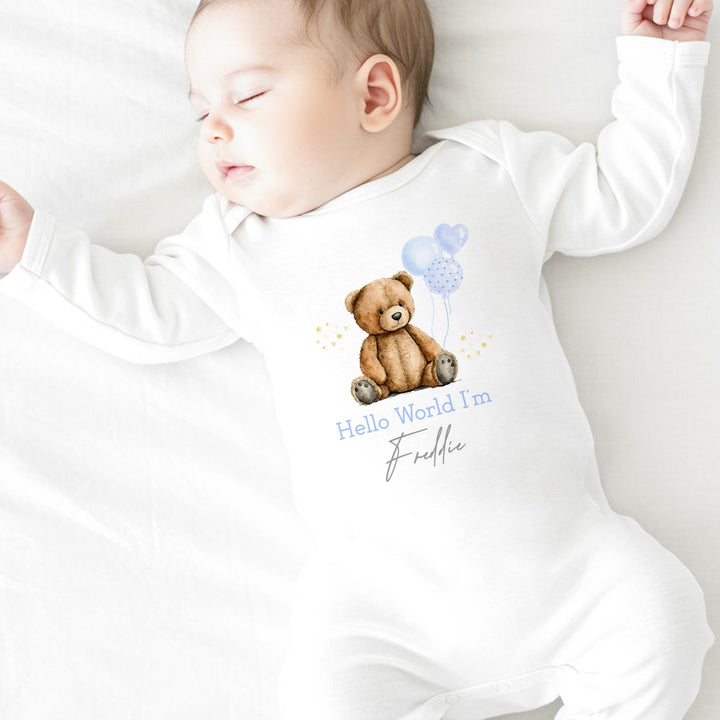 a personalised white baby grow that says 'Hello World I'm Freddie'. This design features a teddy bear holding a blue bunch of blue balloons