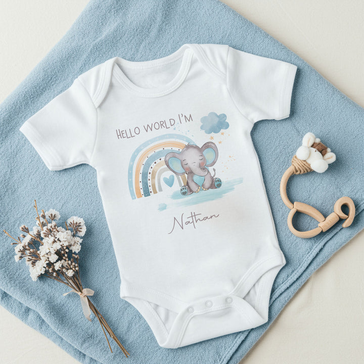 Personalised white baby vest that says 'Hello World I'm Nathan'. This design features a blue rainbow with an elephant in front it 