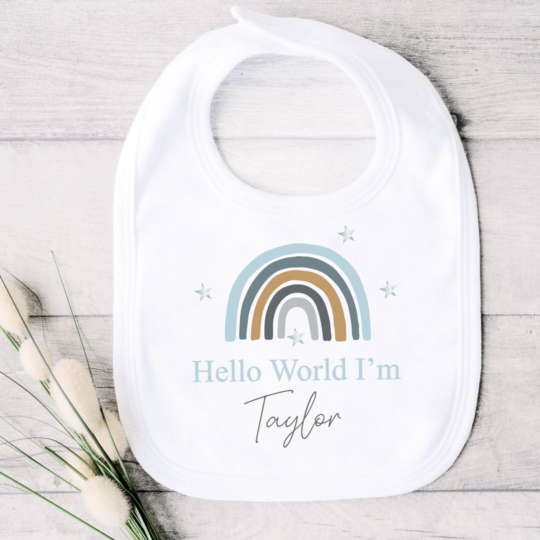 a personalised white baby vest that says 'Hello World I'm Taylor'. This design features a blue rainbow