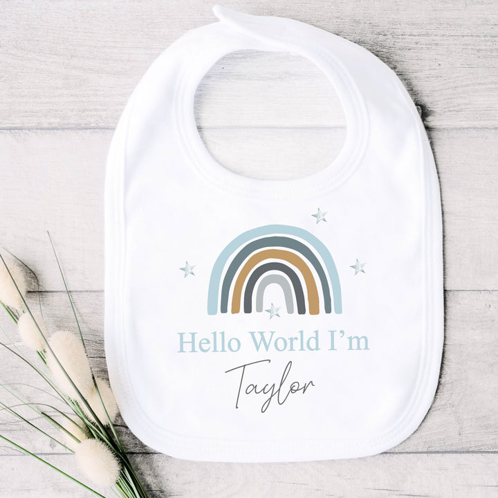 a personalised white baby vest that says 'Hello World I'm Taylor'. This design features a blue rainbow