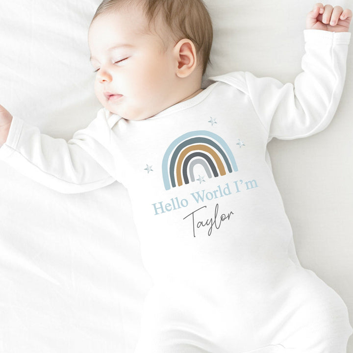 a personalised white baby grow that says 'Hello World I'm Taylor'. This design features a blue rainbow
