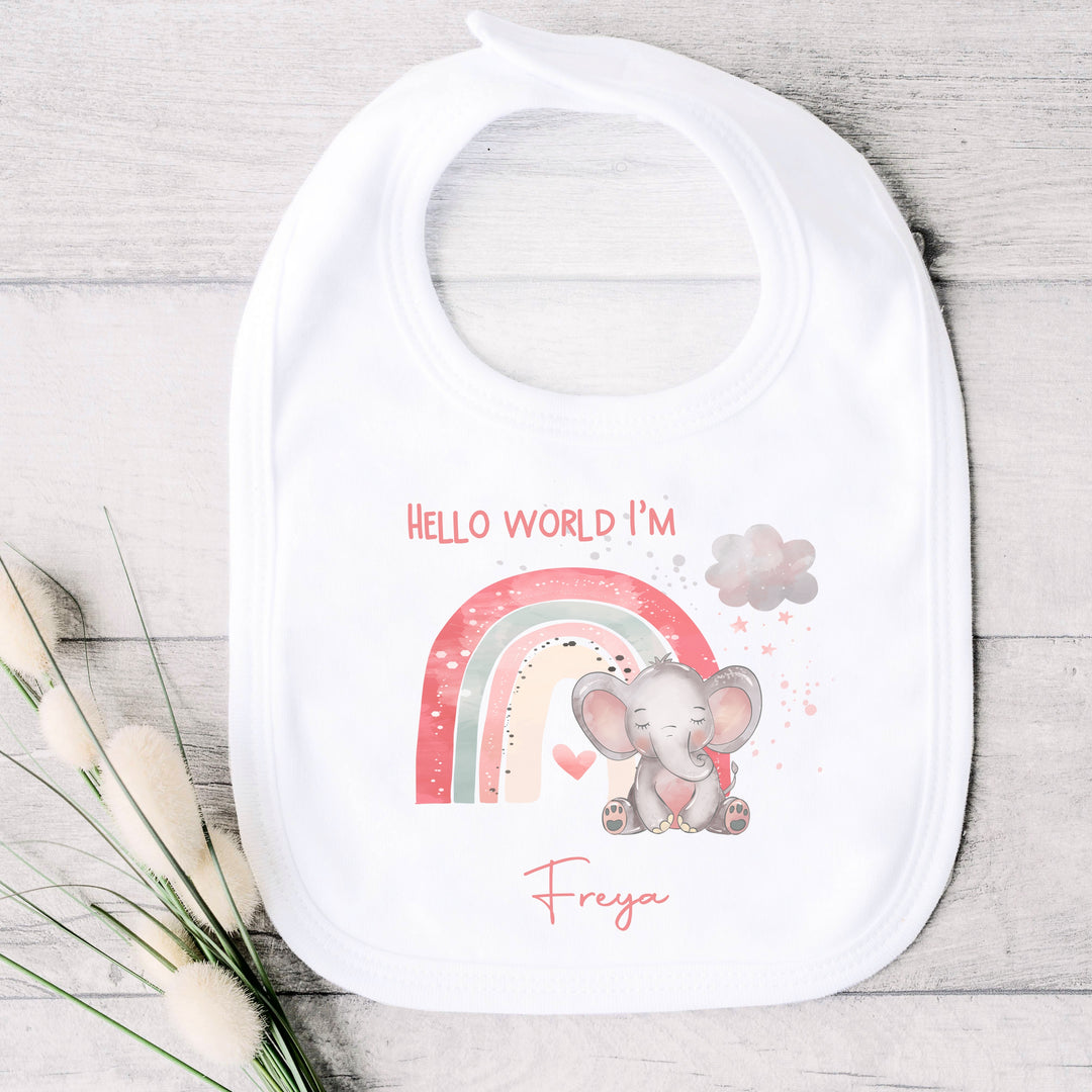 personalised white baby bib that says 'Hello world I'm Freya'. This design features a pink rainbow with an elephant sitting in front of it