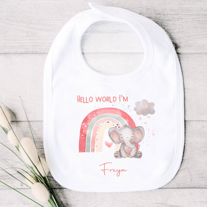 personalised white baby bib that says 'Hello world I'm Freya'. This design features a pink rainbow with an elephant sitting in front of it