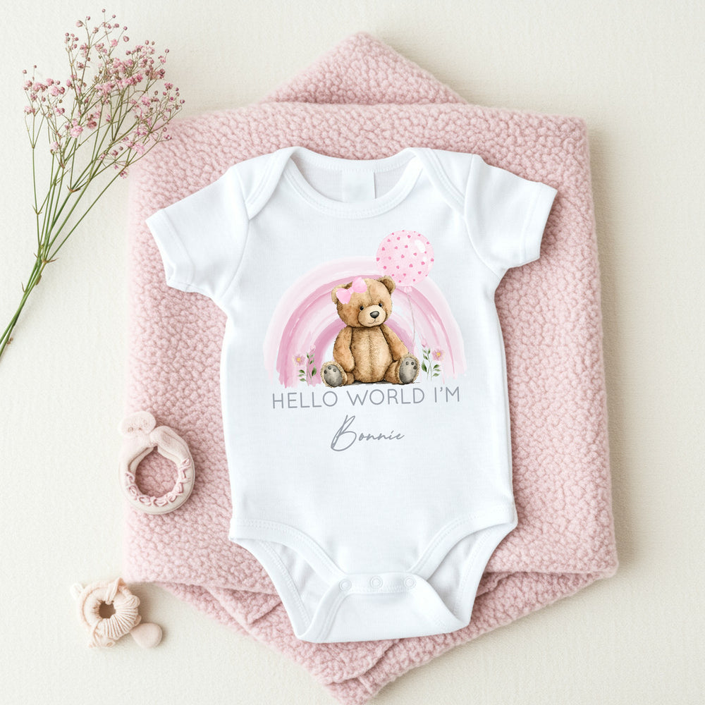 a personalised white baby vest that says 'Hello World I'm Bonnie'. This design features a pink rainbow with teddy infront of it 
