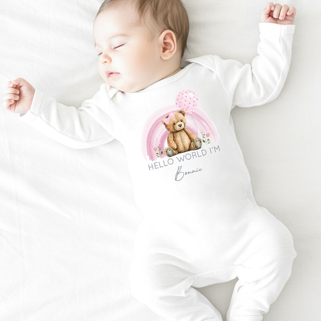 a personalised white baby grow that says 'Hello World I'm Bonnie'. This design features a pink rainbow with teddy infront of it 