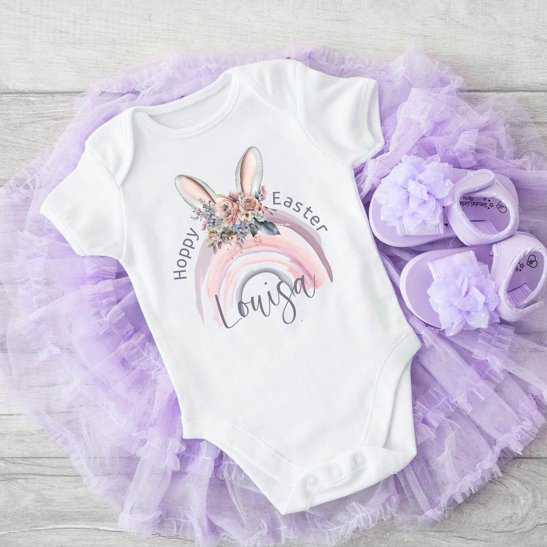 Personalised white Easter baby vest that says 'Hoppy Easter Louisa'. This design features a purple rainbow with bunny ears on top