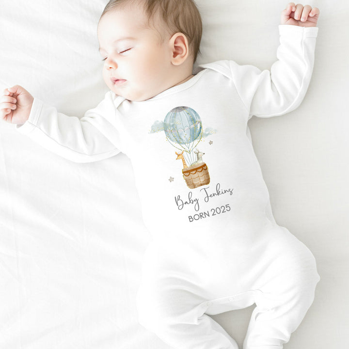 a personalised white baby grow that says 'Baby Jenkins Born 2025'. This design features a blue hot air balloon