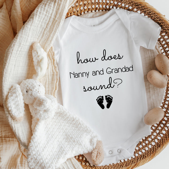 Baby announcement vests that says: 'how does Nanny and Grandad sound?' with two baby feet at the bottom