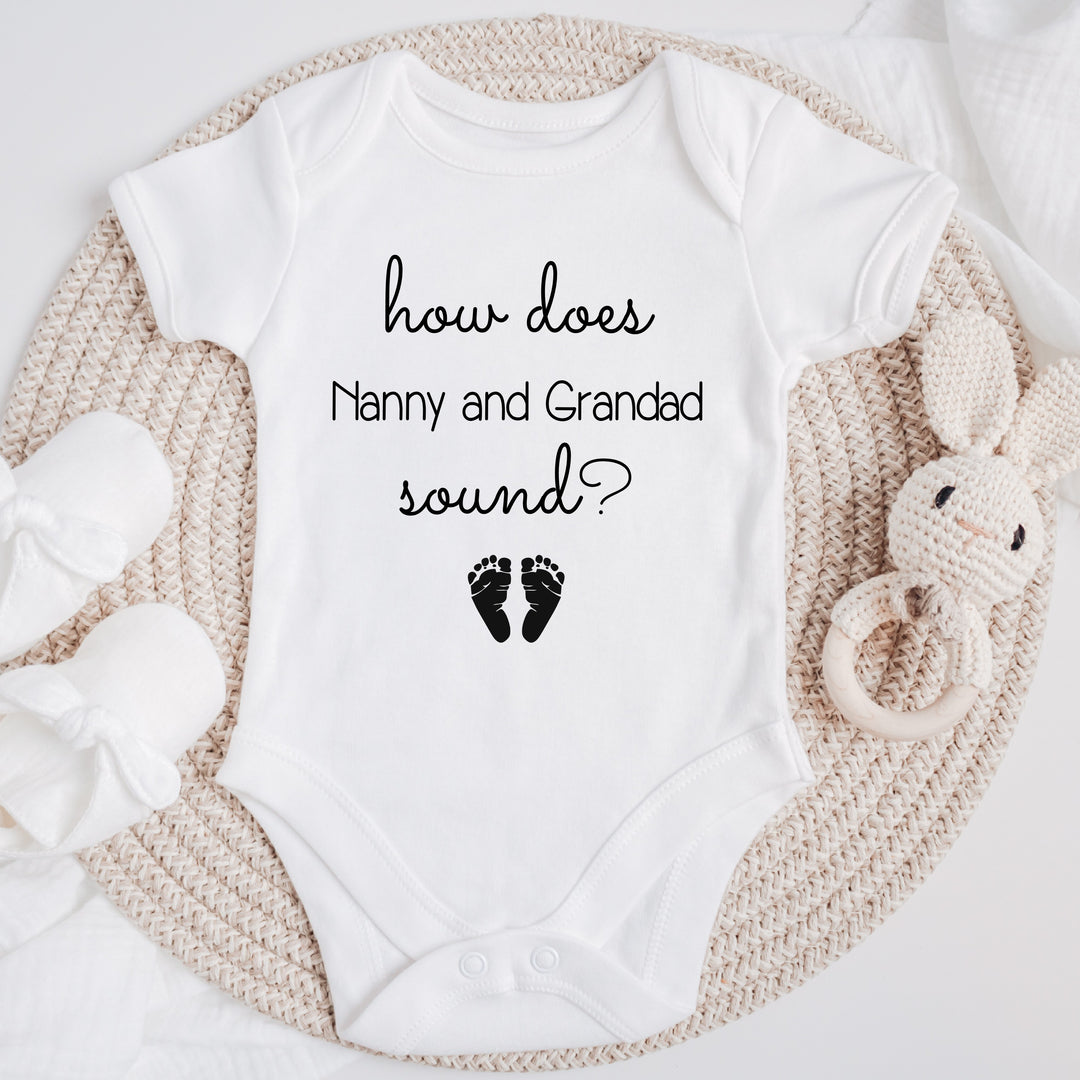 Baby announcement vests that says: 'how does Nanny and Grandad sound?' with two baby feet at the bottom