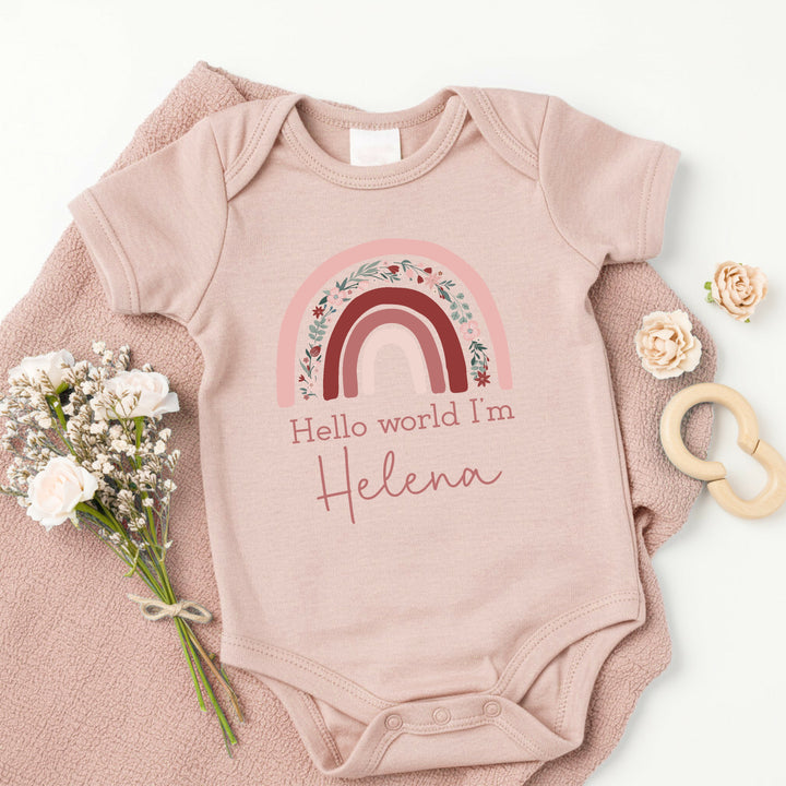 a personalised pink baby vest that says 'Hello World I'm Helena'. This design features a pink floral rainbow 