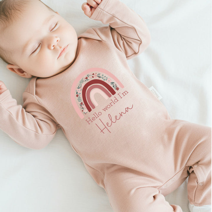 a personalised pink baby grow that says 'Hello World I'm Helena'. This design features a pink floral rainbow 