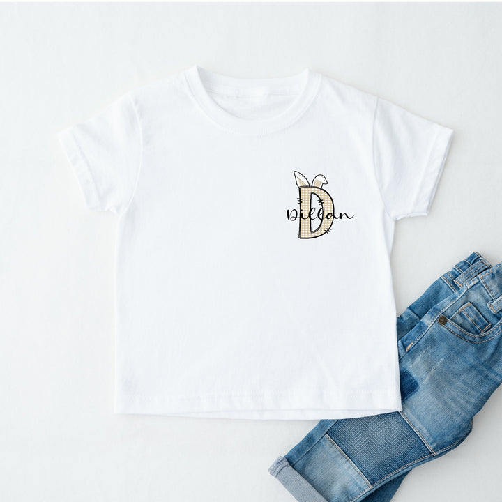 Personalised white Easter t-shirt that says 'D Dillan'. This design features a beige tartan D with bunny ears