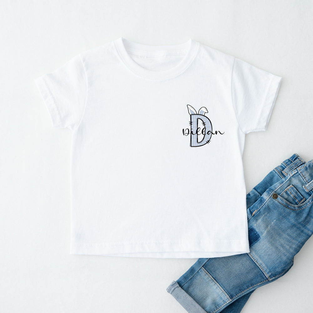 Personalised white Easter t-shirt that says 'D Dillan'. This design features a blue tartan D with blue bunny ears on it 