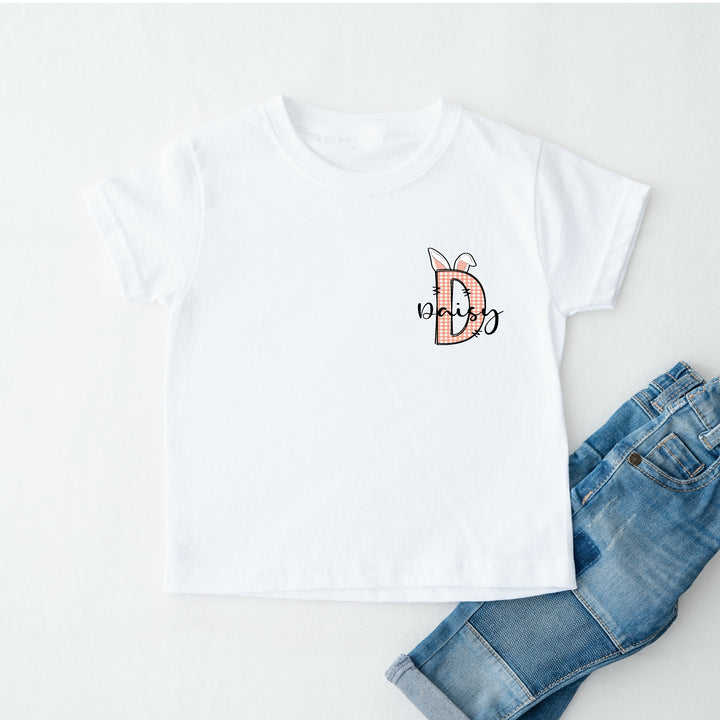 Personalised white Easter t-shirt that says 'D Daisy'. This design features a pink tartan D with bunny ears