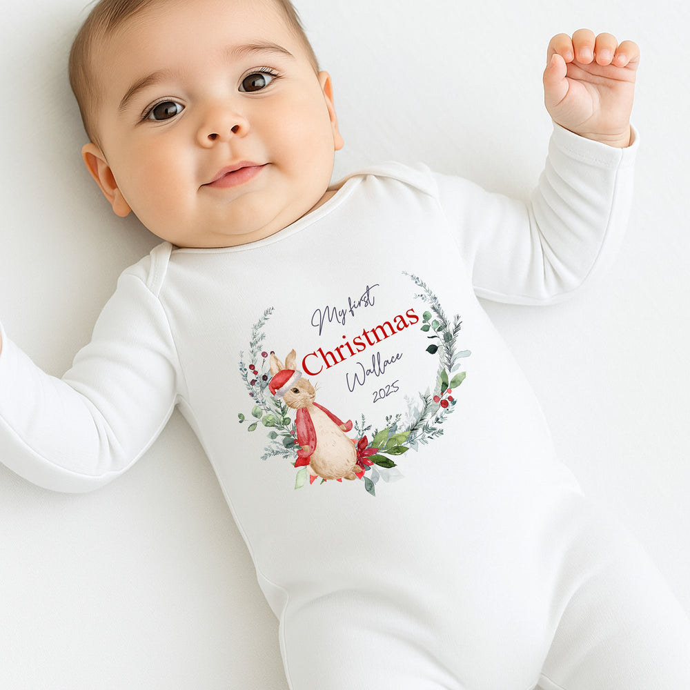 Baby wearing a white onesie with a Christmas design and text.