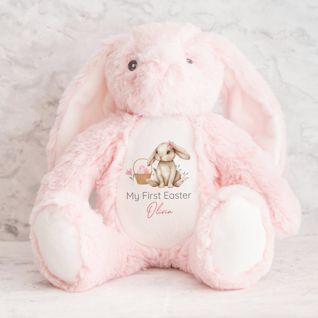 Personalised pink bunny Easter teddy that says 'My First Easter Olivia'. This design features a brown bunny wearing a pink bow sitting next to an Easter basket full of pink Easter eggs