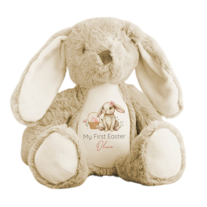 Personalised beige bunny Easter teddy that says 'My First Easter Olivia'. This design features a brown bunny wearing a pink bow sitting next to an Easter basket full of pink Easter eggs