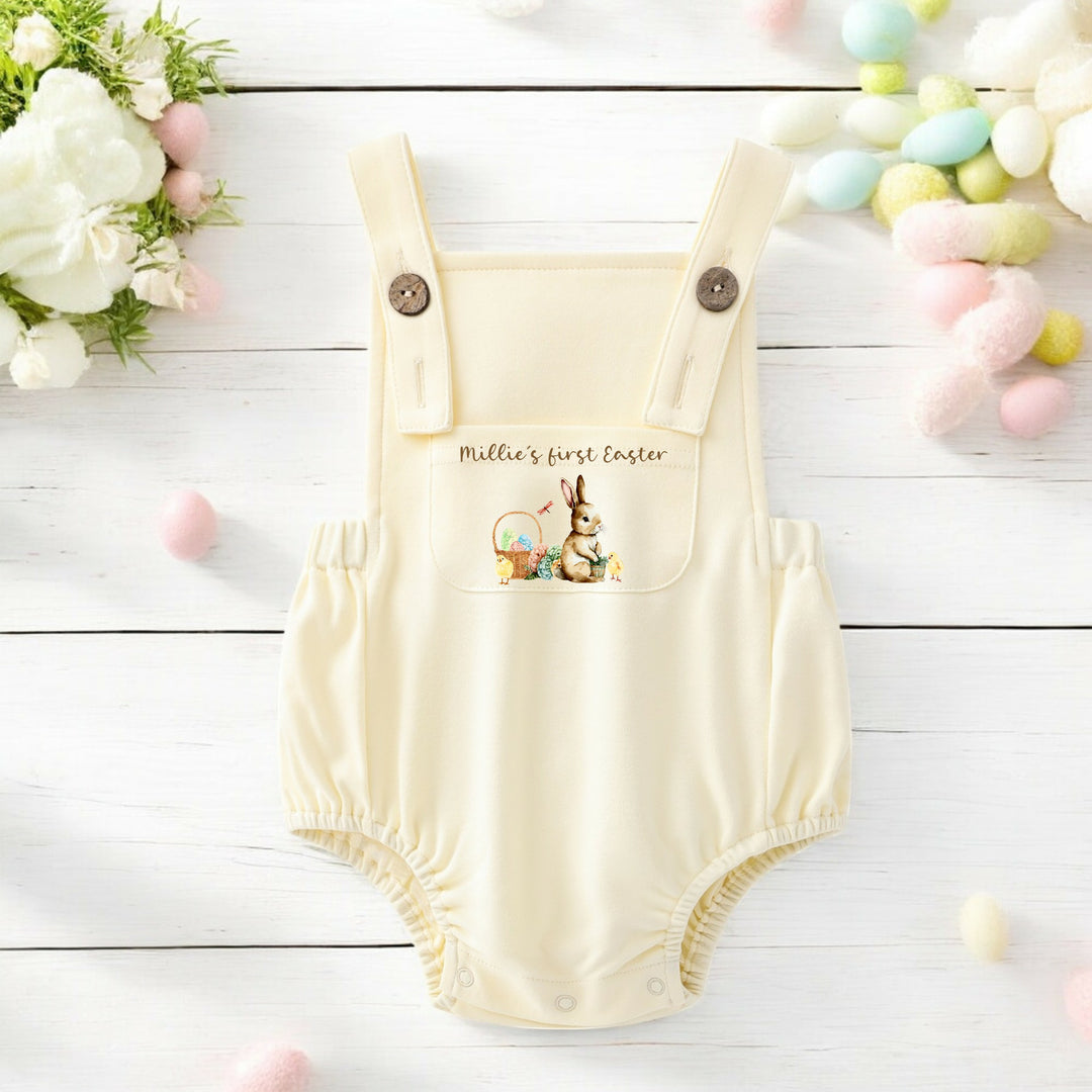 Personalised lemon Easter dungarees that say 'Millie's First Easter'. This design features a brown bunny sittinhg next to an Easter basket full of eggs