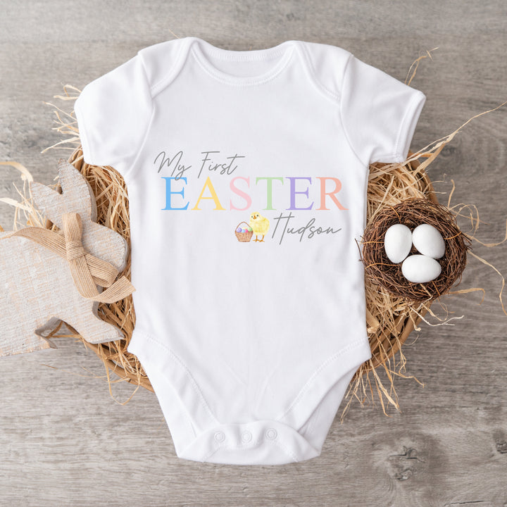 Personalised white Easter baby vest that says 'My First Easter Hudson'. This design features a yellow chick