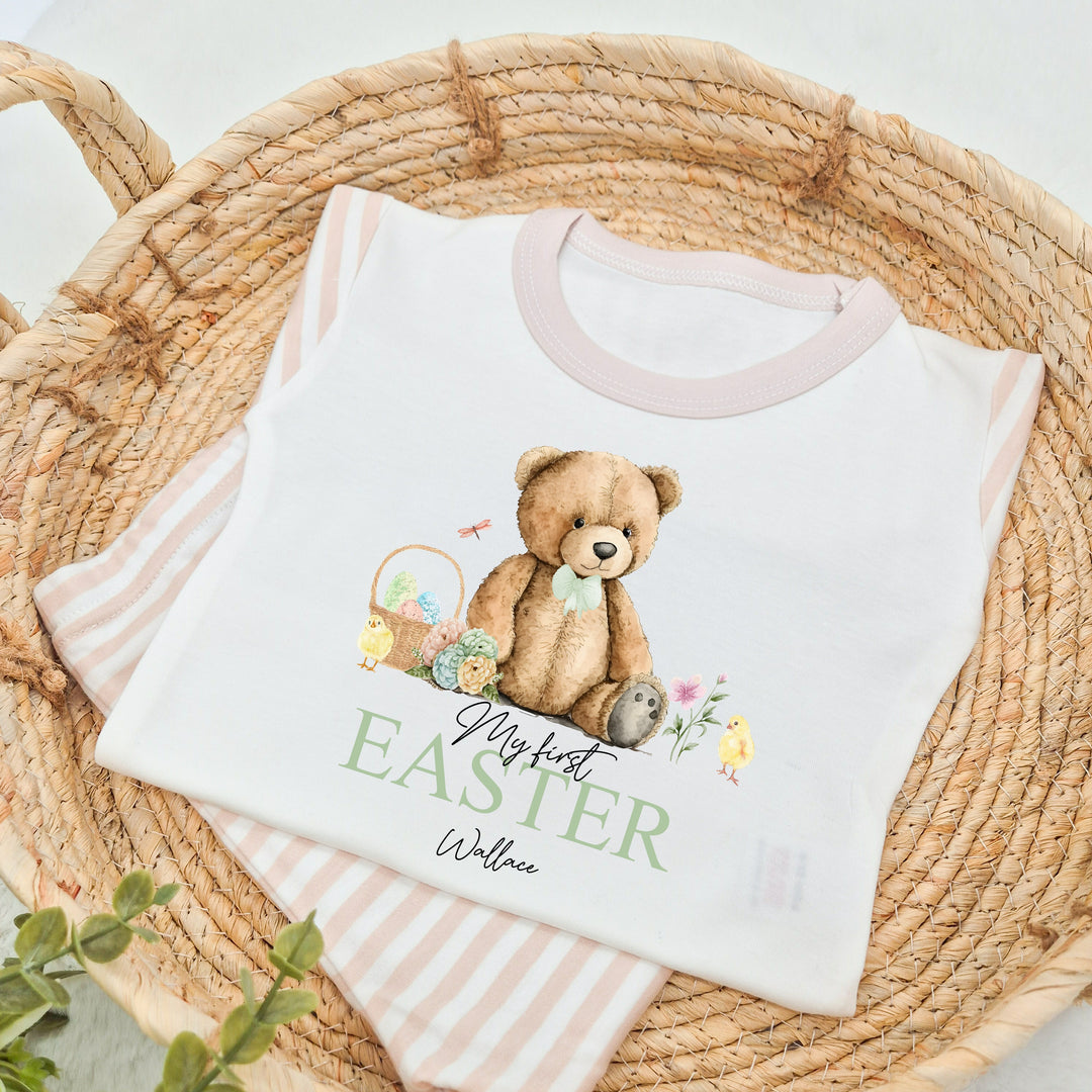 Personalised beige stripe Easter pyjamas that say 'My first EASTER Wallace'. This design features a teddy bear wearing a sage green bow tie surrounded by Easter eggs