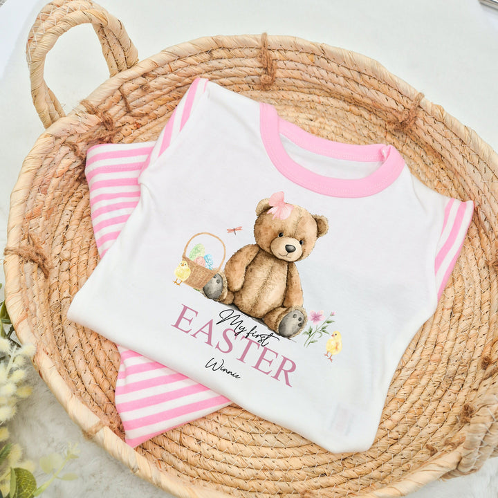 Peronalised pink stripe Easter pyjamas that say 'My First Easter Winnie'. This design features a teddy wearing a pink bow surrounded by an easter basket