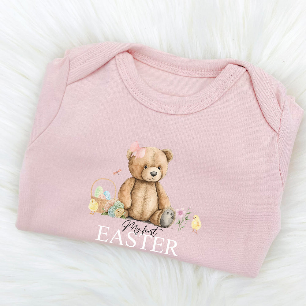 Personalised pink Easter baby grow/sleepsuit that says 'My First Easter Winnie'. This design features a teddy bear wearing a bow sitting next to an Easter basket and 2 yellow chicks