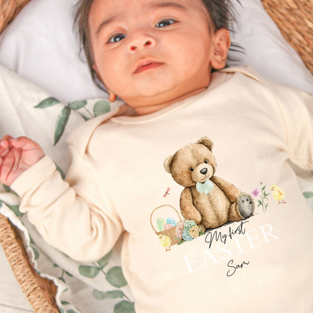 Peronalised beige Easter baby grow/sleepsuit that says 'My First Easter Sam'. This design features a teddy bear wearing a sage green bow tie sitting with an Easter basket and 2 chicks