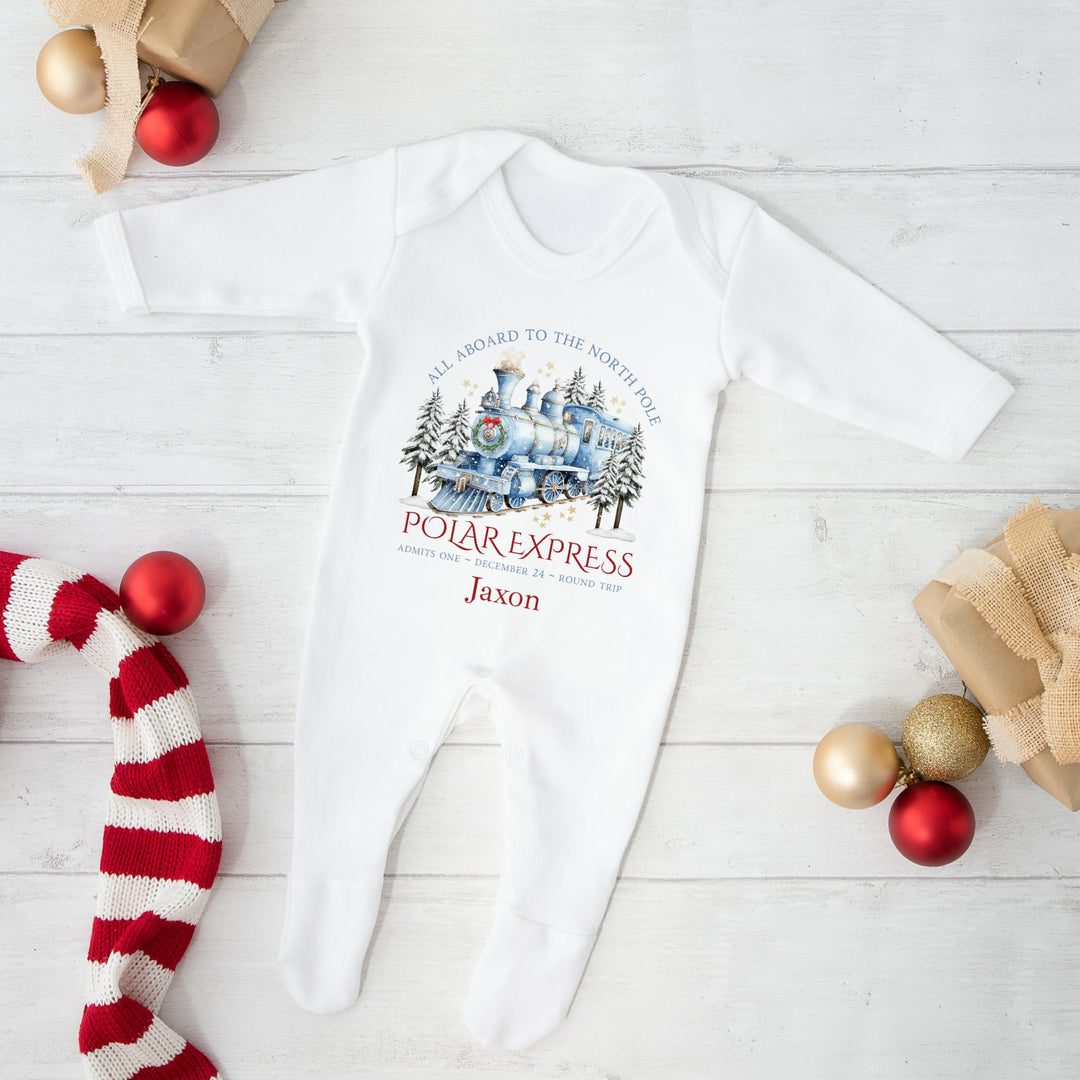 White baby onesie with 'Polar Express' design on a white wooden surface with Christmas decor.