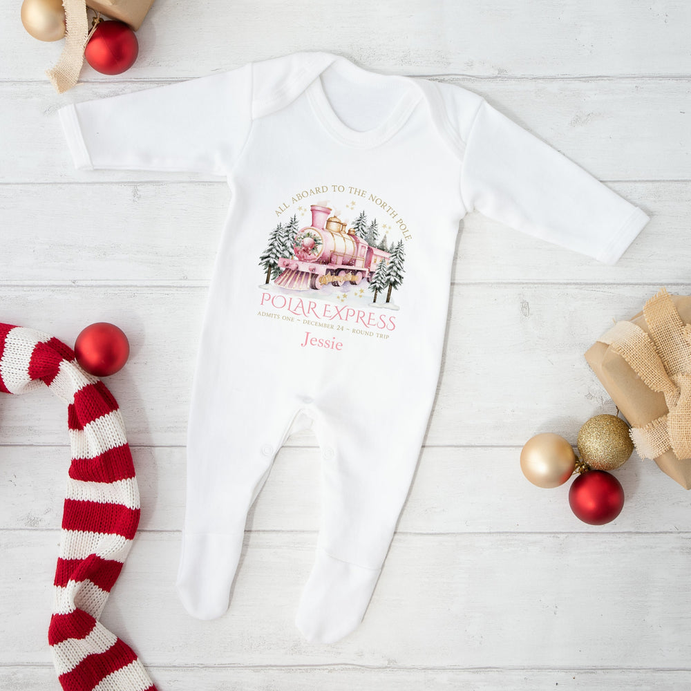 White baby onesie with 'Polar Express' design on a white wooden surface with Christmas decor.