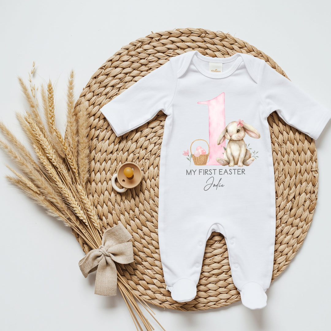 Personalised white Easter baby grow/sleepsuit that says 'My First Easter Jodie'. This design features a big pink 1 with a brown bunny one side and an Easter basket the other side