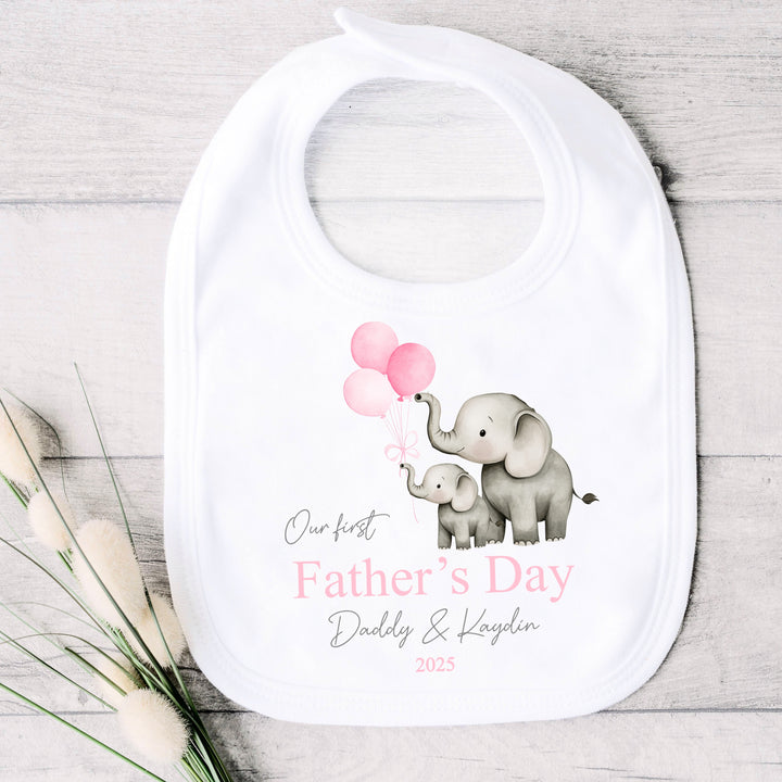 Personalised white Father's Day baby bib  that says 'Our First Father's Day Daddy & Kaydin 2025'. This design features 2 grey elephants holding 3 pink balloons