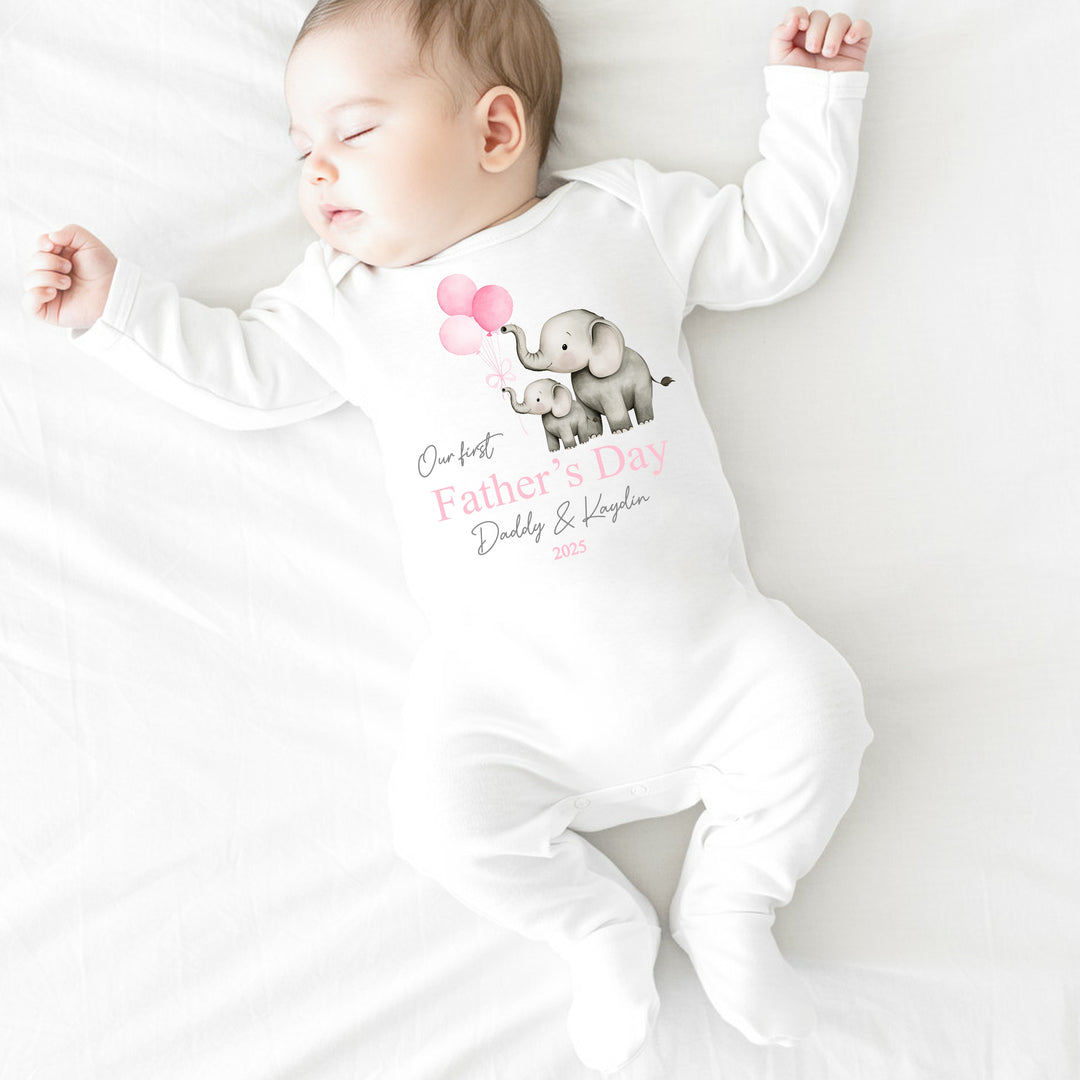 Personalised white Father's Day baby grow/sleepsuit that says 'Our First Father's Day Daddy & Kaydin 2025'. This design features 2 grey elephants holding 3 pink balloons