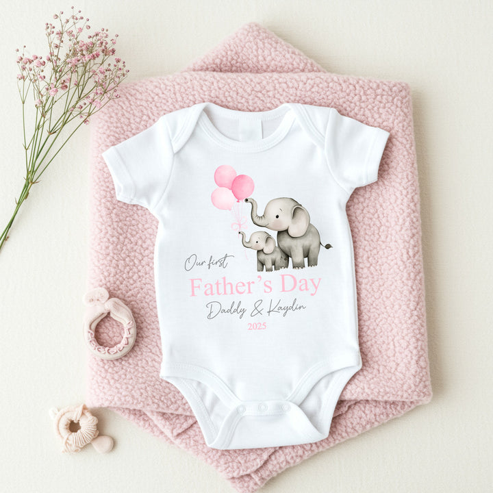 Personalised white Father's Day baby vest that says 'Our First Father's Day Daddy & Kaydin 2025'. This design features 2 grey elephants holding 3 pink balloons