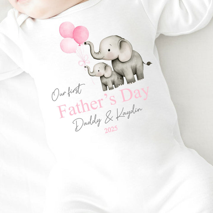 Personalised white Father's Day baby grow/sleepsuit that says 'Our First Father's Day Daddy & Kaydin 2025'. This design features 2 grey elephants holding 3 pink balloons