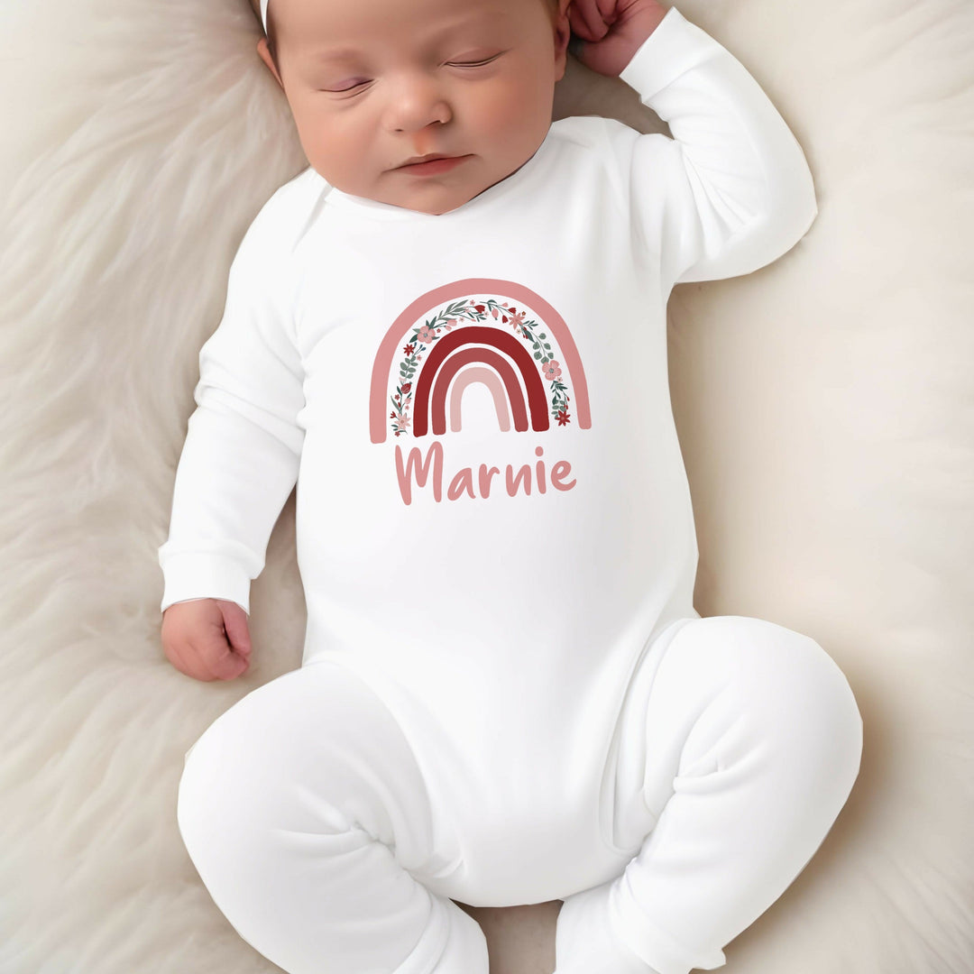 a personalised white baby grow that says 'Marnie'. This design features a pink floral rainbow