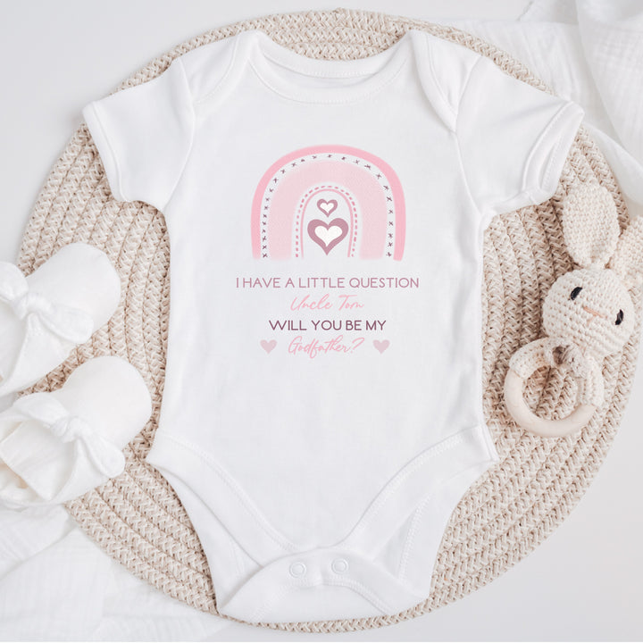 Baby announcement vests that says: 'I have a little question Uncle Tom Will you be my godfather?' This is in pink text with a pink rainbow above the text