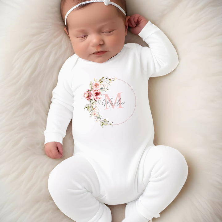 A personalised white baby grow that says 'Annabelle'. This design features a pink floral wreath with a name and initial in the middle