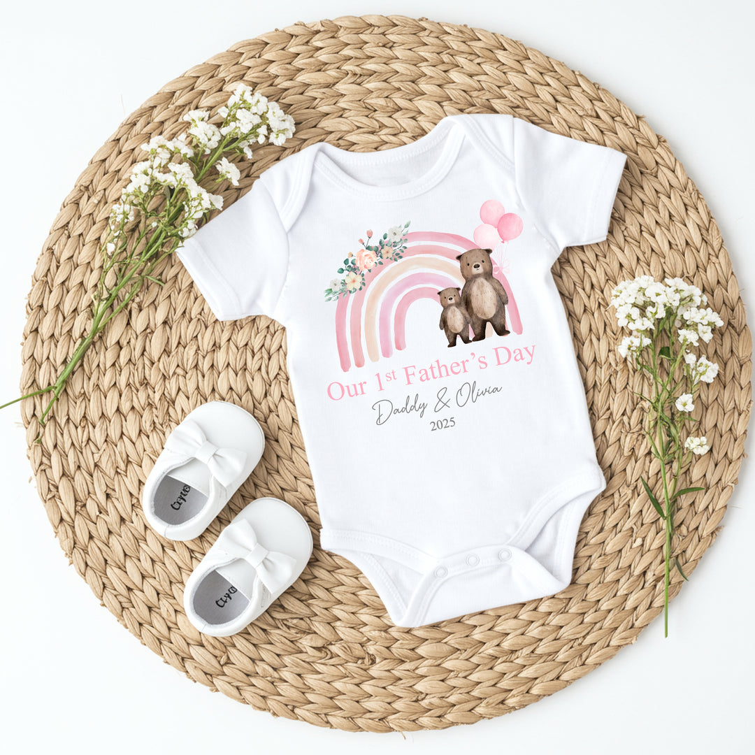 Personalised white Father's Day baby vest that says 'Our 1st Father's Day Daddy & Olivia 2025'. This design features a pink rainbow with 2 bears holding 3 pink balloons