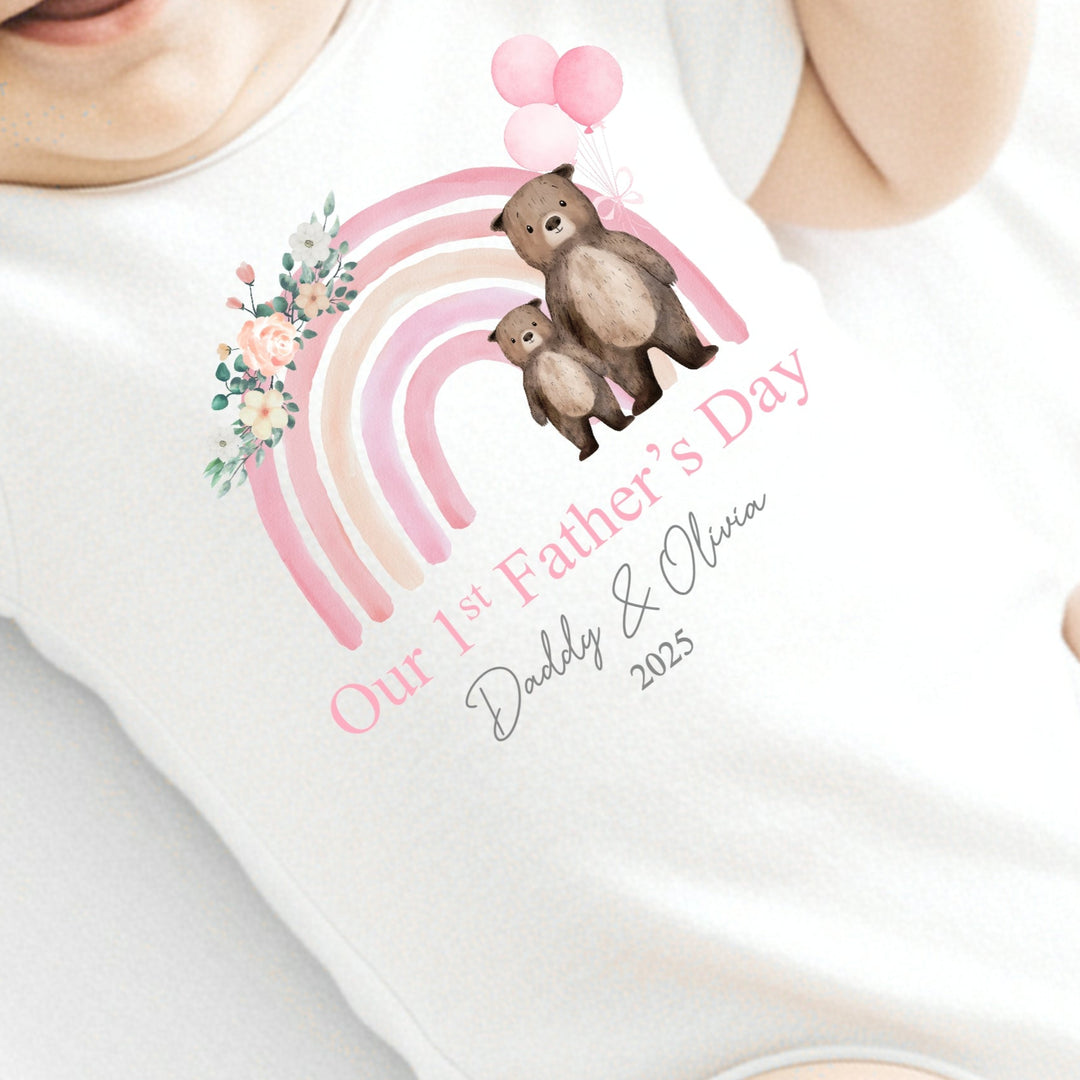 Personalised white Father's Day baby vest that says 'Our 1st Father's Day Daddy & Olivia 2025'. This design features a pink rainbow with 2 bears holding 3 pink balloons