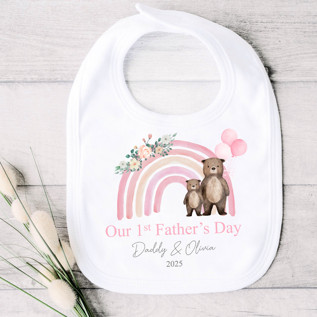 Personalised white Father's Day baby bib that says 'Our 1st Father's Day Daddy & Olivia 2025'. This design features a pink rainbow with 2 bears holding 3 pink balloons