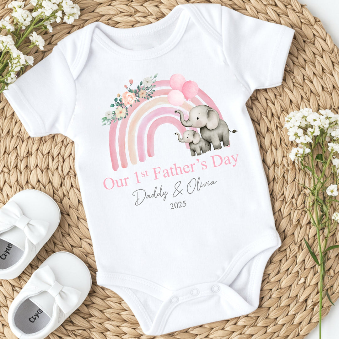 Personalised white Father's Day baby vest that says 'Our 1st Father's Day Daddy & Olivia 2025'. This design features a pink rainbow with 2 grey elephants holding 3 pink balloons