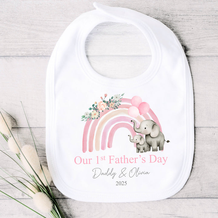 Personalised white Father's Day baby bib that says 'Our 1st Father's Day Daddy & Olivia 2025'. This design features a pink rainbow with 2 grey elephants holding 3 pink balloons