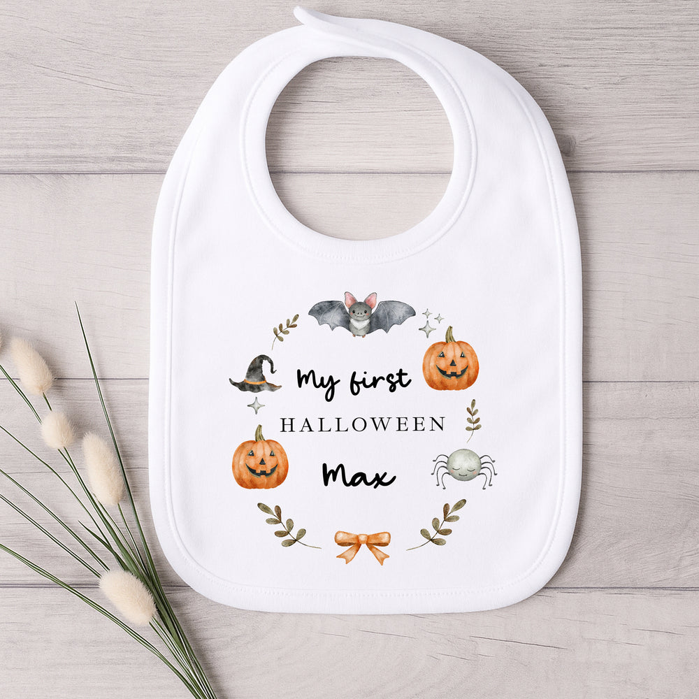 Baby bib with Halloween-themed design and text on a wooden surface