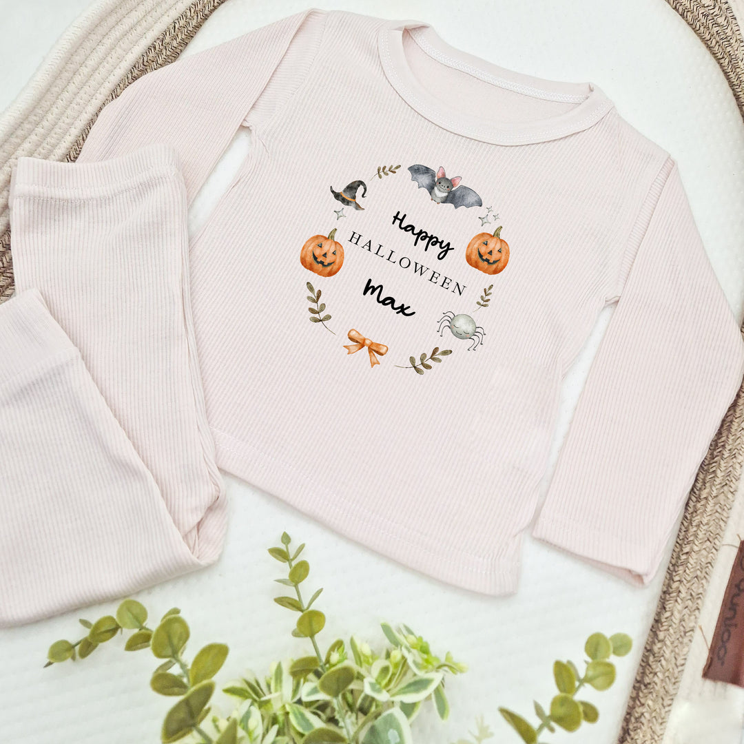 Pink baby outfit with 'Happy Halloween Max' text and pumpkin design on a white surface.