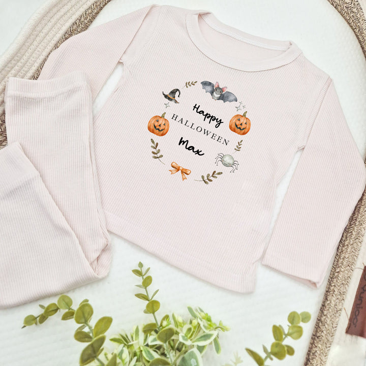 Pink baby outfit with 'Happy Halloween Max' text and pumpkin design on a white surface.